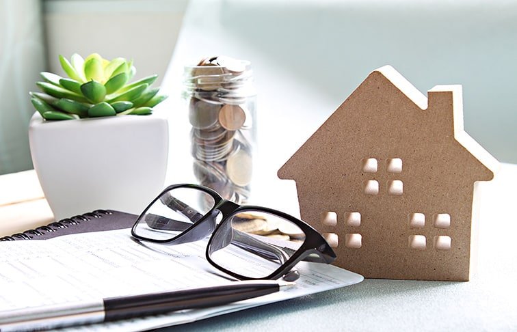 Real Estate Jobs image showing a house model, coin savings jar, eyeglasses, notebook, and pen used for property investment and financial planning.